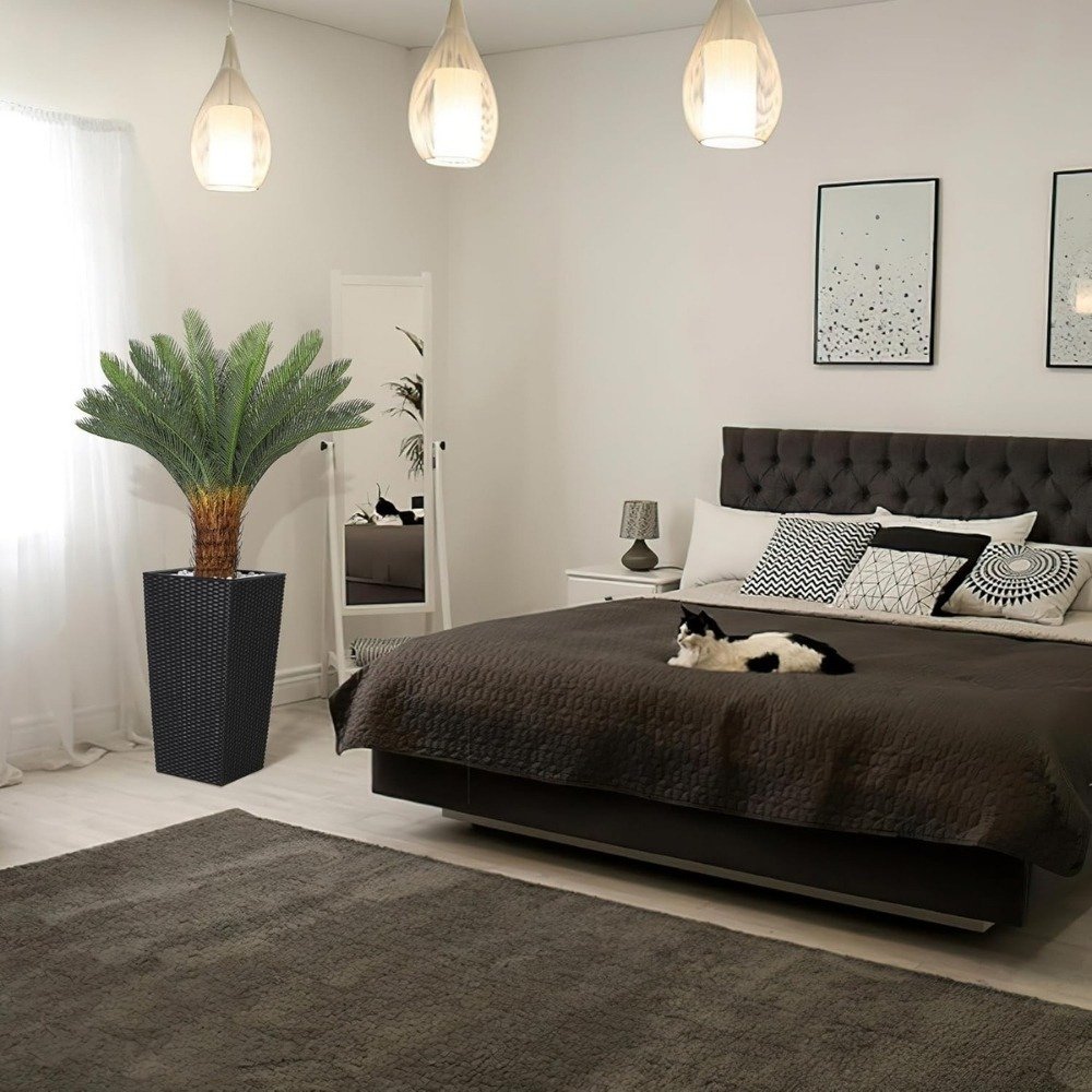 Artificial sago palm tree in a black pot placed in a modern bedroom setting with warm lighting