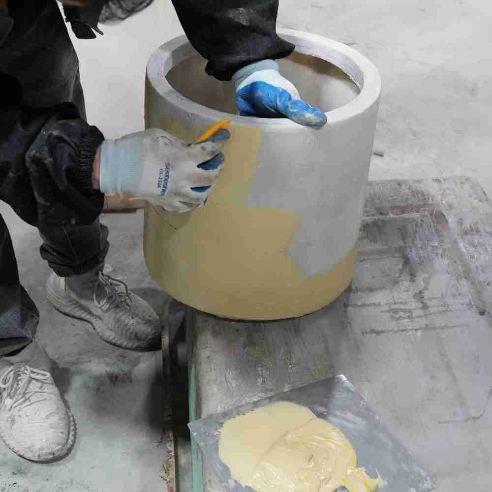 Close-up of the manual finishing and smoothing process for a bespoke cylindrical planter, ensuring a premium surface quality for commercial landscape projects.