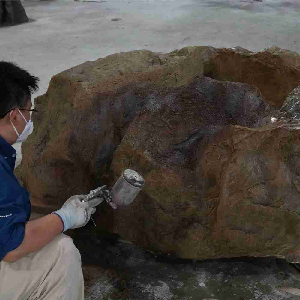 A skilled Oakco artisan using a spray gun to apply realistic color gradients and natural textures to a custom-fabricated artificial rock base.