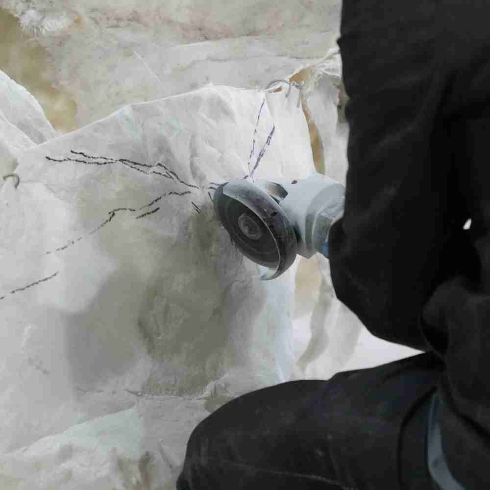 A technician using a handheld grinder to refine the cracks and organic details of an artificial rock, creating a hyper-realistic geological look.