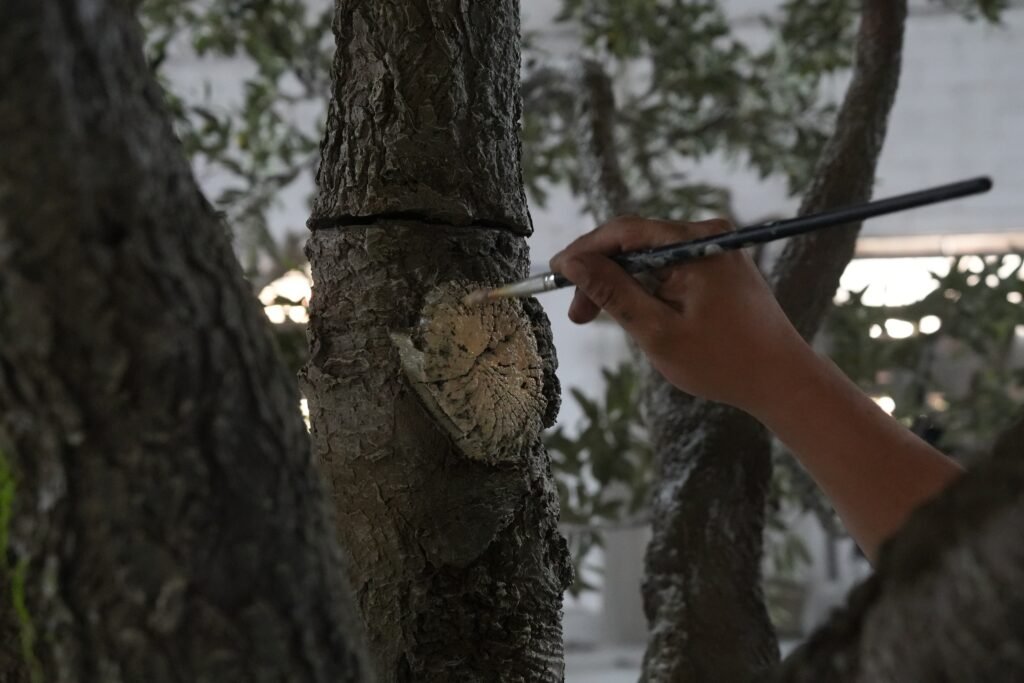 Close-up of an artist meticulously hand-painting realistic bark textures and knots on an artificial tree trunk to ensure a hyper-realistic botanical finish.