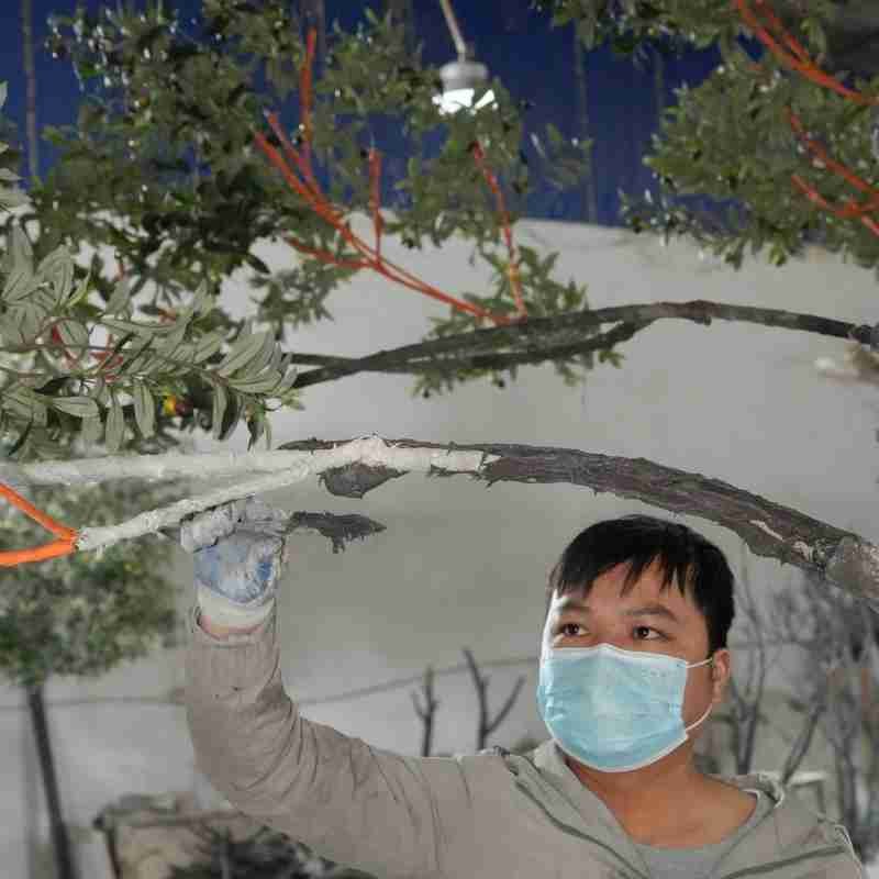 Worker applying fiberglass finishing to the branches of a custom artificial olive tree