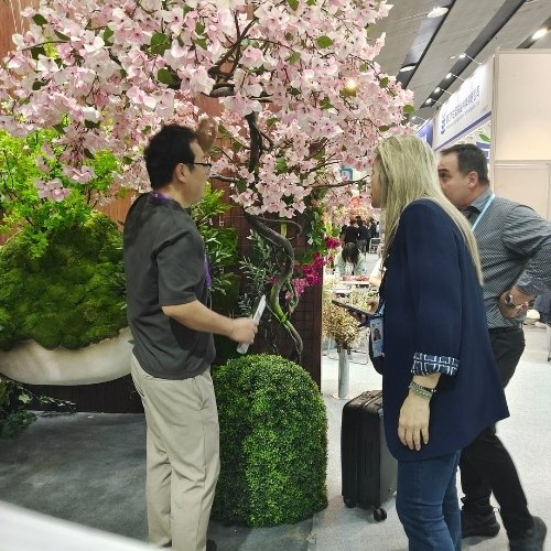 Oakco representative presenting artificial cherry blossom trees, topiary, and custom artificial landscaping solutions to visitors at the Canton Fair booth.