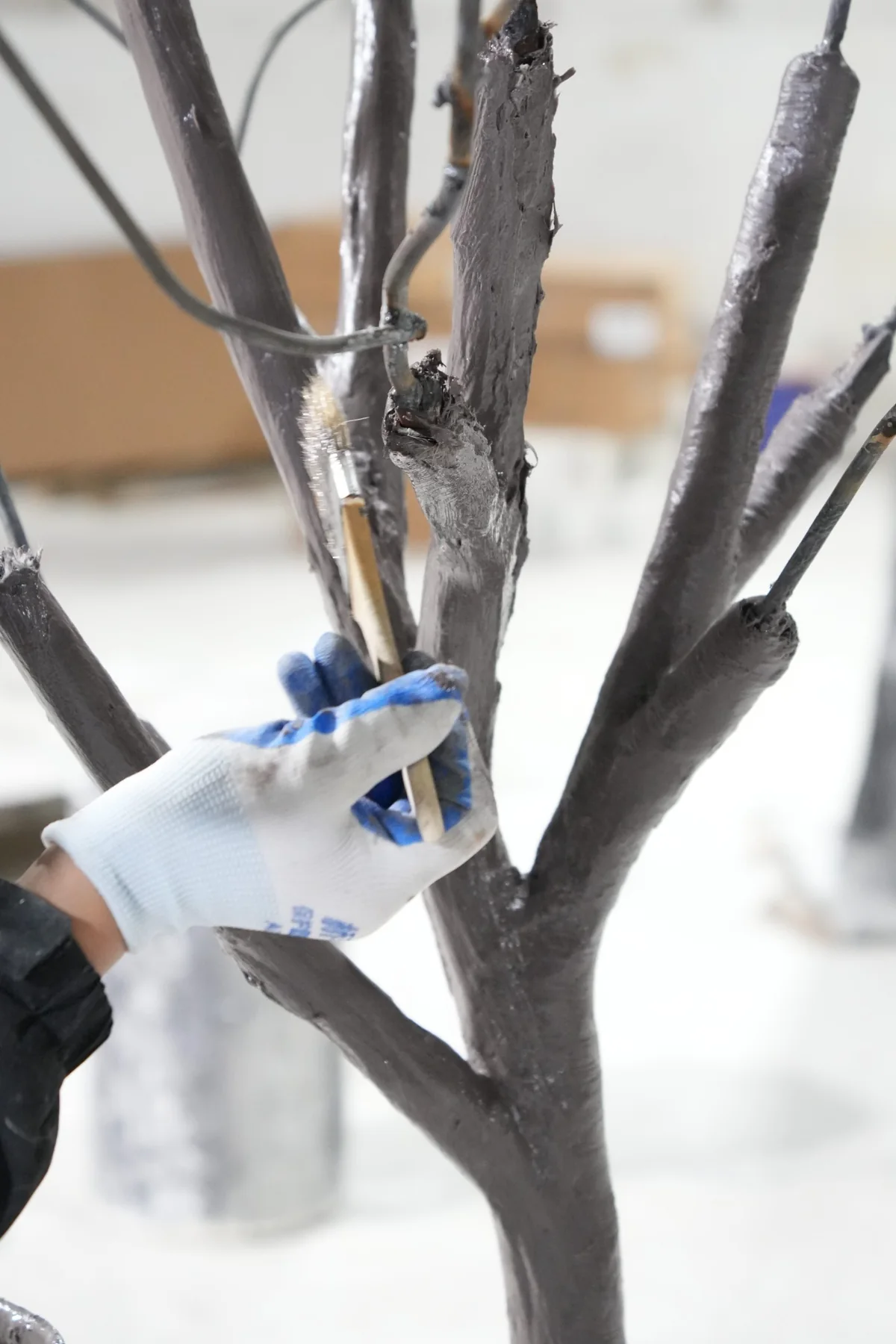 Close-up of a craftsman coating fiberglass-reinforced artificial orange tree branches by hand