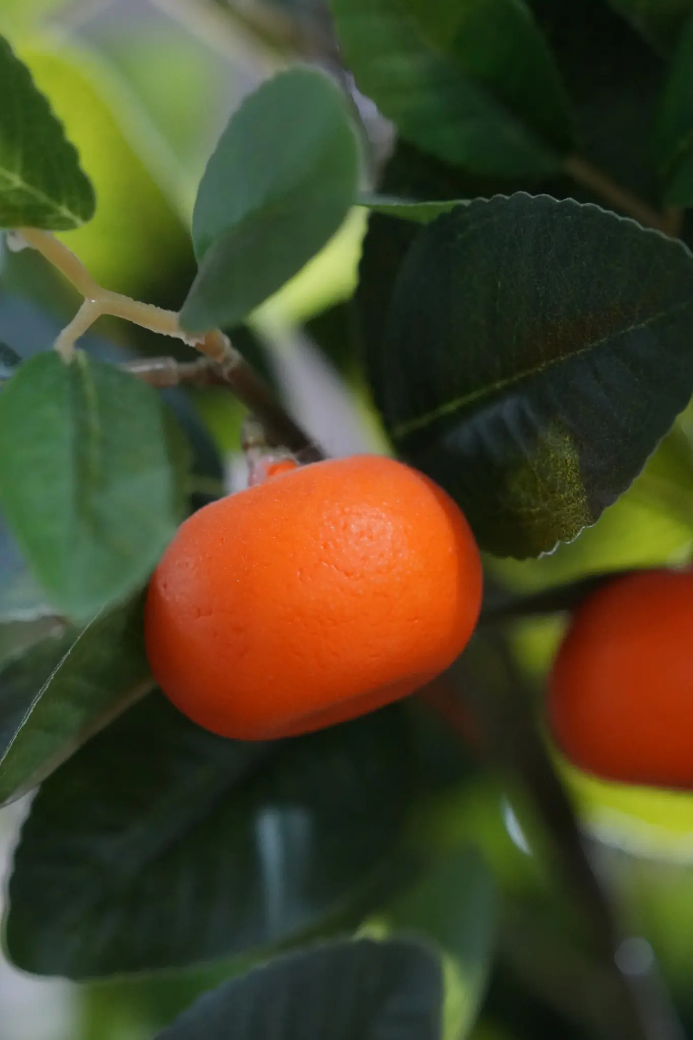 Close-up of artificial orange fruit with detailed surface texture and surrounding leaves