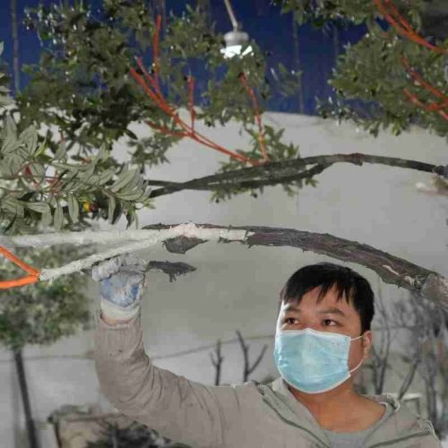 Worker applying fiberglass finishing to the branches of a custom artificial olive tree
