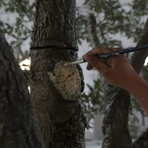 Close-up of an artist meticulously hand-painting realistic bark textures and knots on an artificial tree trunk to ensure a hyper-realistic botanical finish.